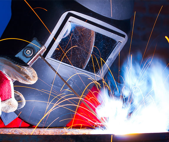 Close up of a welder working on a part while sparks and smoke emit from the heated elements