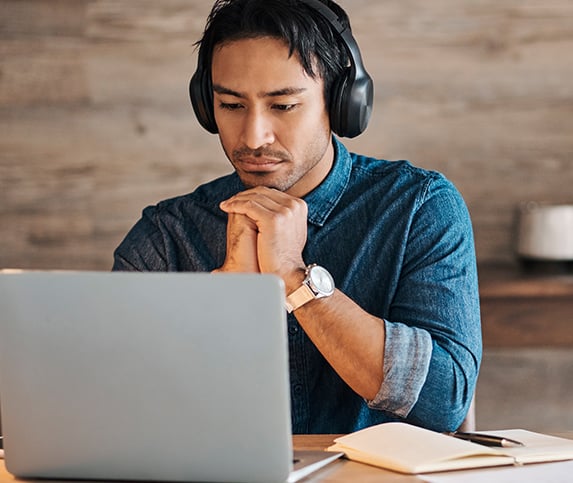 middle-aged man with headphones sits in front of a laptop while taking online training from Tooling U-SME
