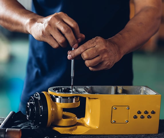 A manufacturing professional’s hands are working on a yellow manufacturing part