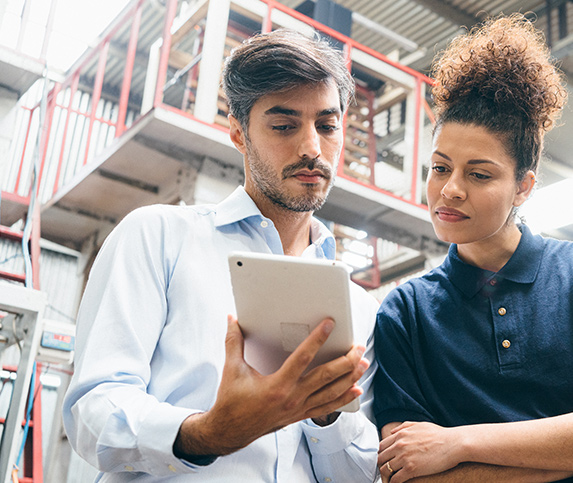 One female and one male workforce professional review upcoming machining jobs on a tablet in a manufacturing plant