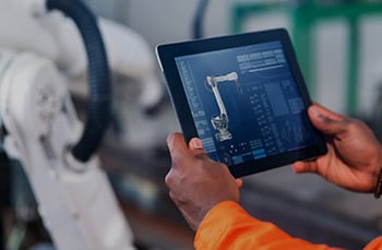 Manufacturing professional holds up a tablet that shows him the status and insights of the machining part as he works within a smart factory.