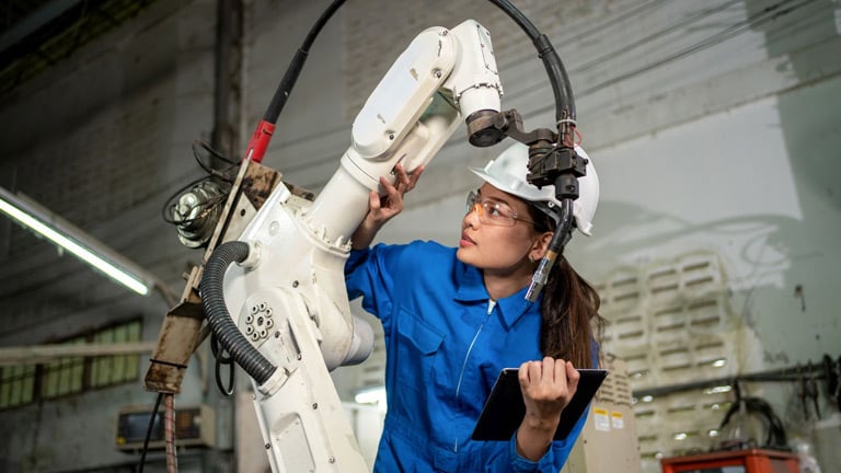 A Female technician with safety glasses performs maintenance on a robot in a manufacturing plant