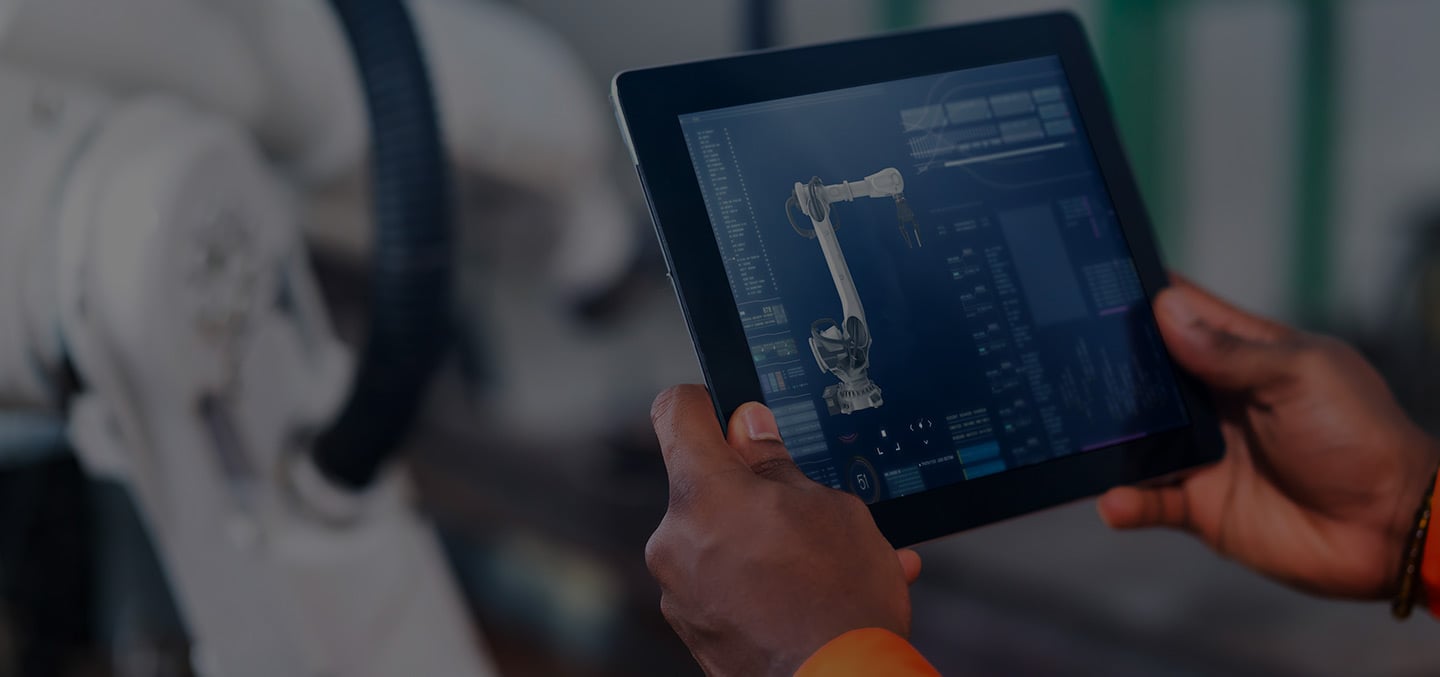 Manufacturing professional holds up a tablet that shows him the status and insights of the machining part as he works within a smart factory.
