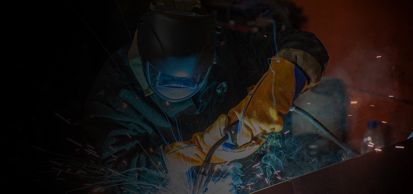welding professional in protective clothing and head gear welds machining part