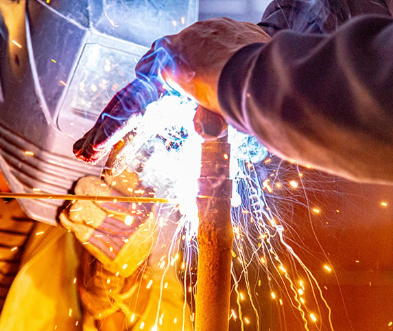 Sparks light up a darkened manufacturing room as welders work on fusing a pipe