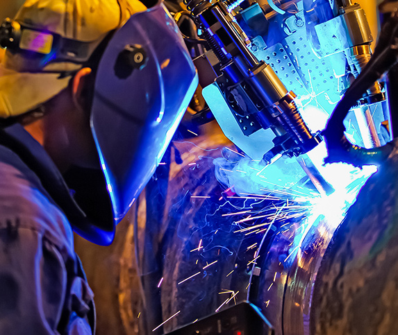 Robotic arm hold a large piece in place while a welding professional welds the part to completion